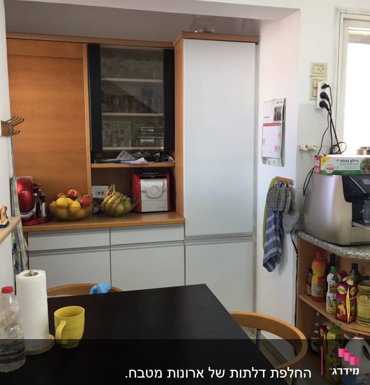 מטבח עם שולחן שחור, כיסאות, ומדפים עם מוצרי מזון.